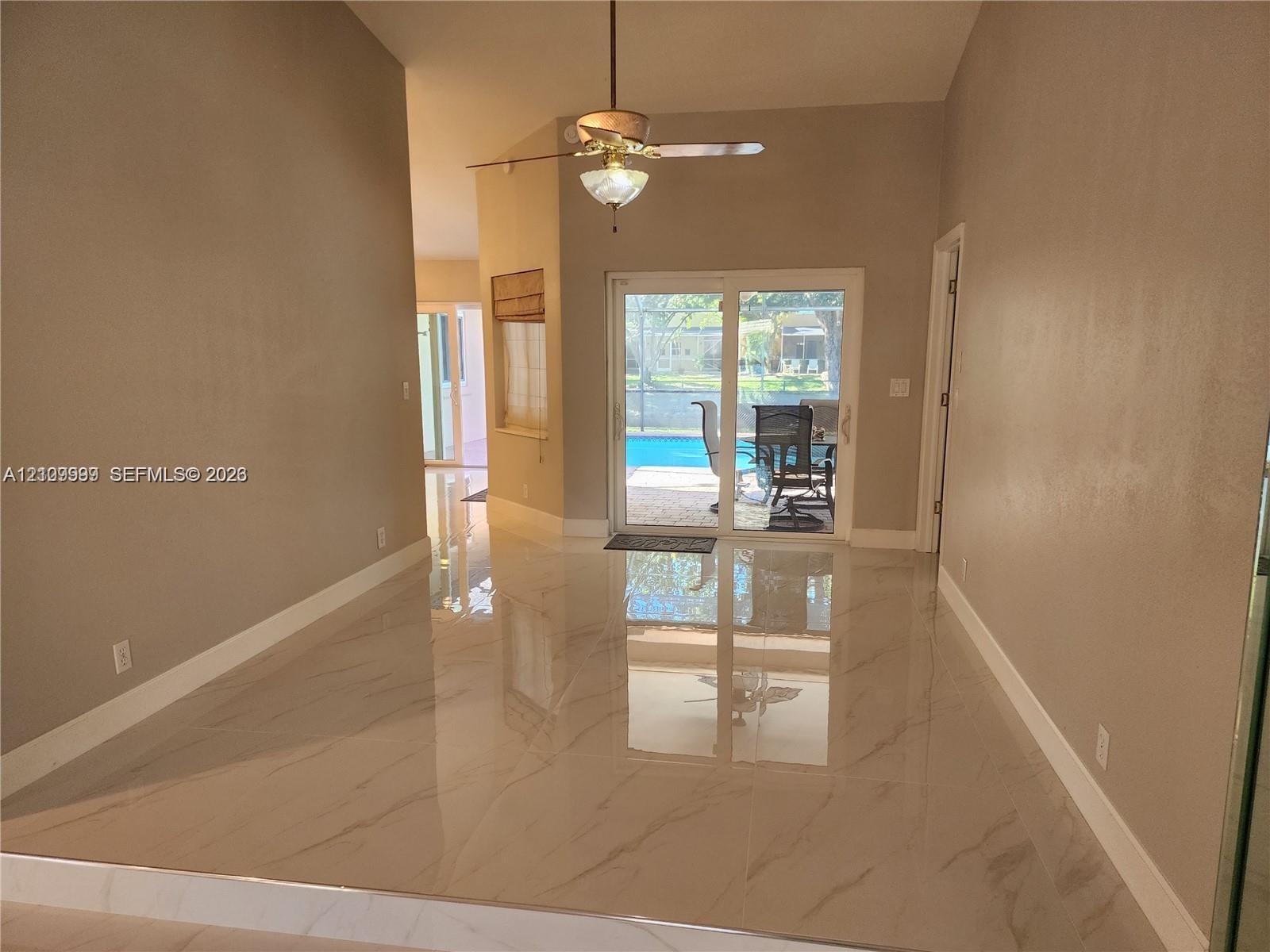 High-ceiling living area featuring large-format polished porcelain tile flooring, sliding glass doors, and a ceiling fan