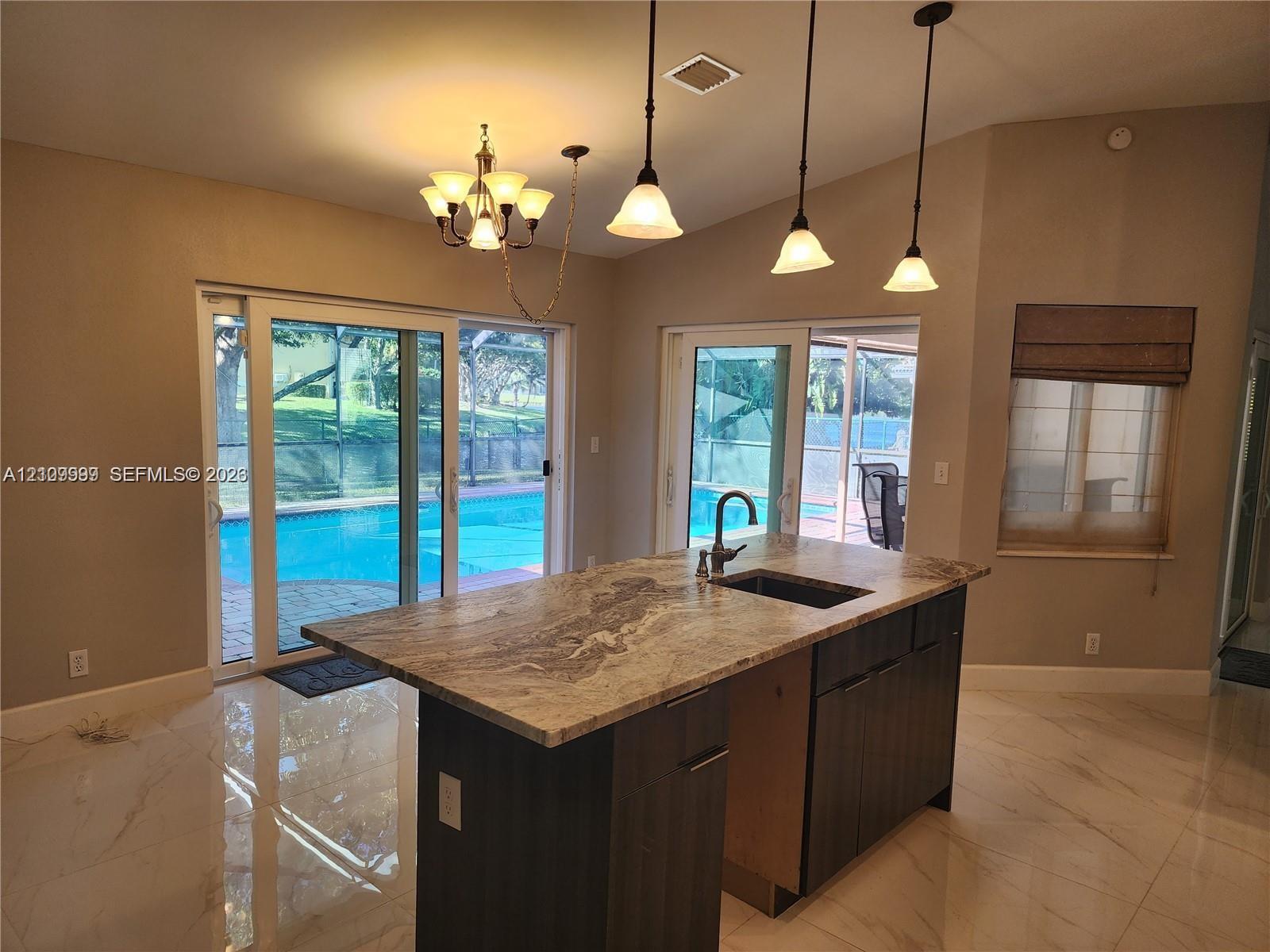 Kitchen featuring an island with a stone countertop, dark wood-finish cabinetry, an undermount sink, a gooseneck faucet, and three pendant light fixtures