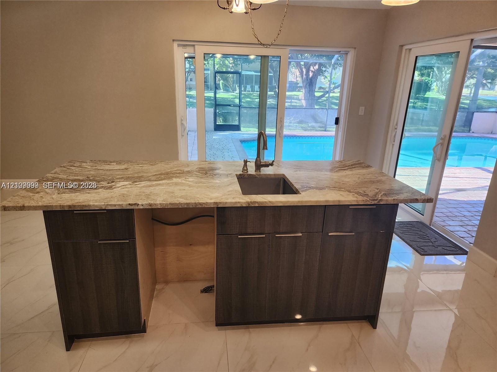 Kitchen island with stone-surface countertop, under-mount sink, high-arc faucet, and dark-finish cabinetry