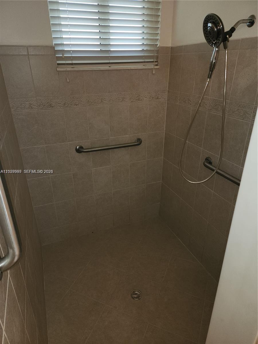 Walk-in shower featuring neutral tile walls, horizontal accent tiling, stainless steel grab bars, and an adjustable handheld showerhead