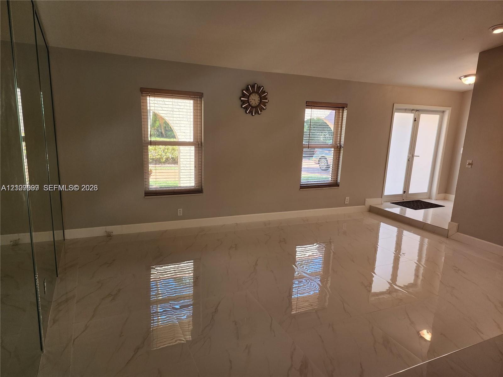 Large-format polished tile flooring, full-height mirrored wall, double-entry glass paneled doors, and dual windows
