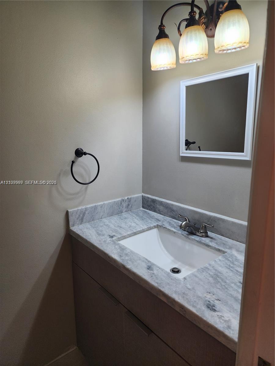 Vanity featuring a stone-surface countertop with an integrated rectangular sink, three-light decorative fixture, framed mirror, and matte black towel ring