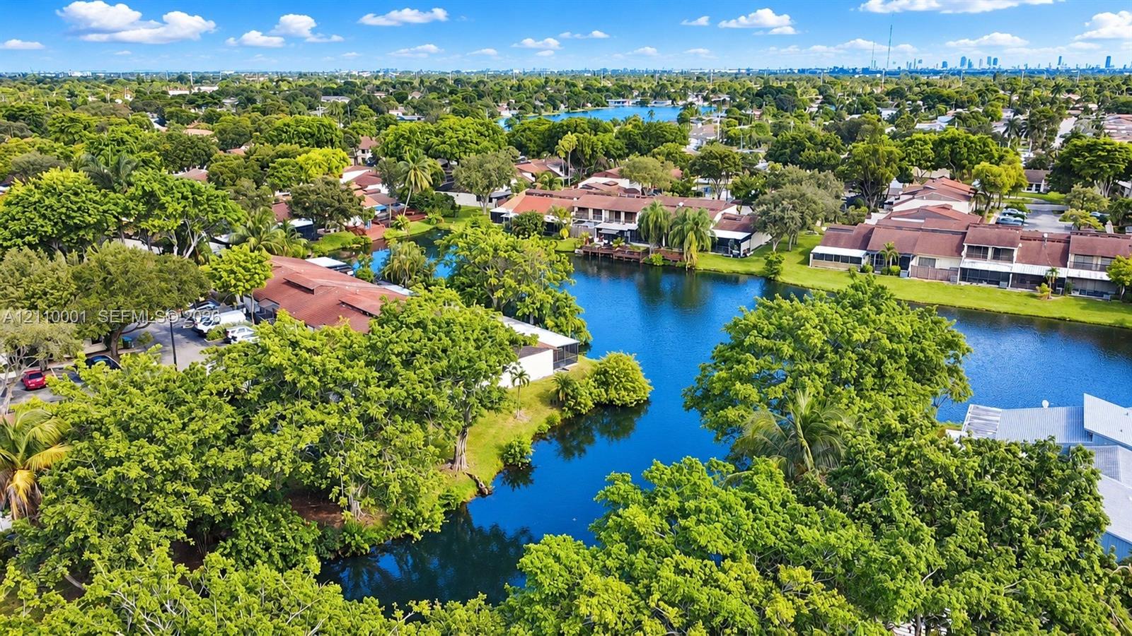 Aerial perspective featuring waterfront property, multi-unit residential structures, red-tiled rooflines, and mature canopy trees