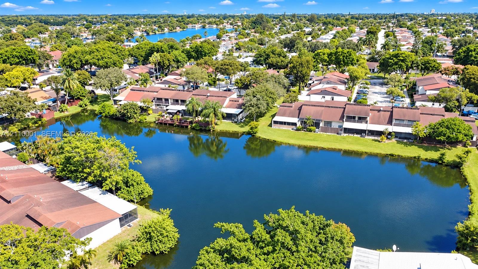 Aerial perspective showcasing expansive water frontage with mature trees, manicured lawns, and multi-level residential structures featuring shingled roofs and enclosed patios