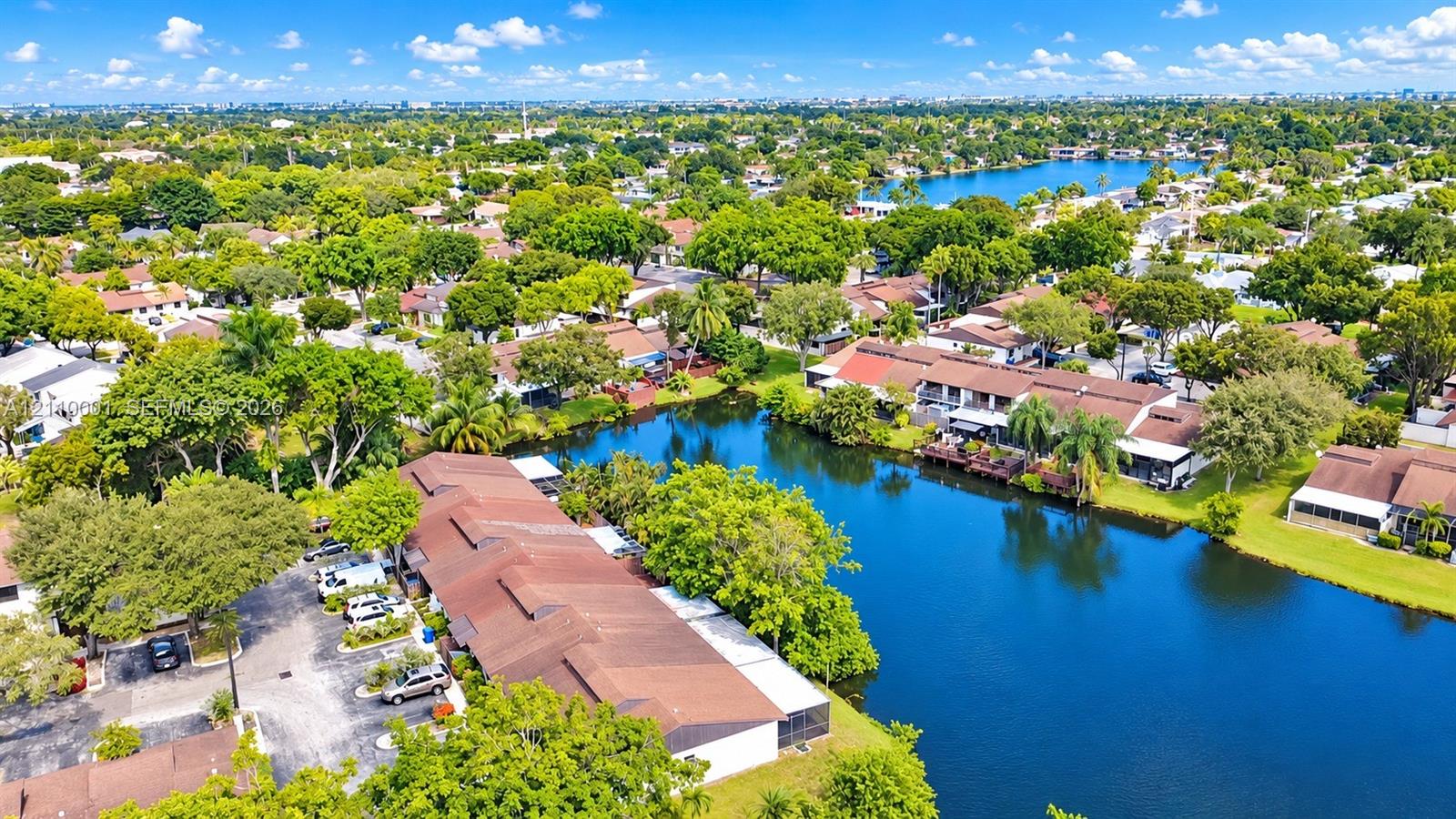 Aerial perspective featuring multi-unit structures with shingle roofing, surface parking, and a prominent water frontage
