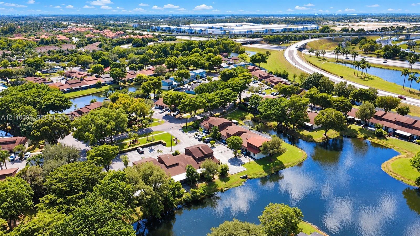 Aerial perspective of a multi-unit residential complex featuring terracotta-tiled rooflines, expansive water features, mature canopy trees, and paved parking areas