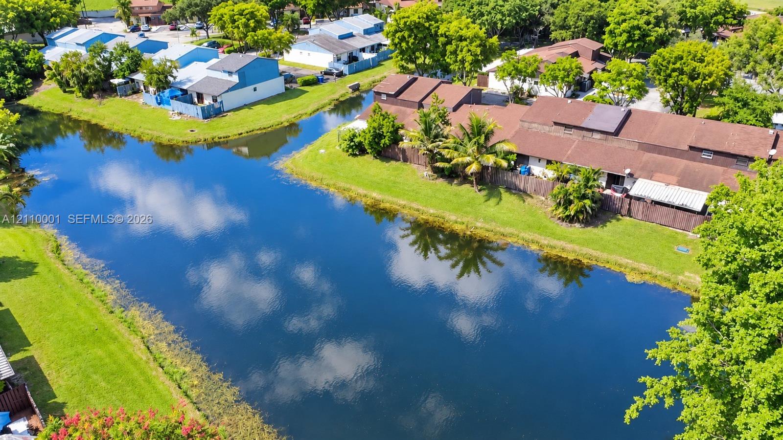 Aerial perspective featuring a waterfront pond, manicured lawn, and mature canopy trees