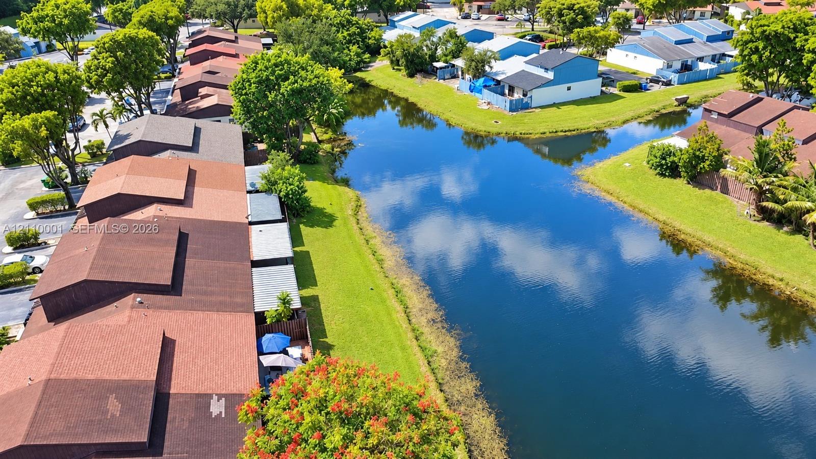 Aerial perspective featuring shingle roofing, residential structures, and a waterway with expansive lawn areas and mature trees