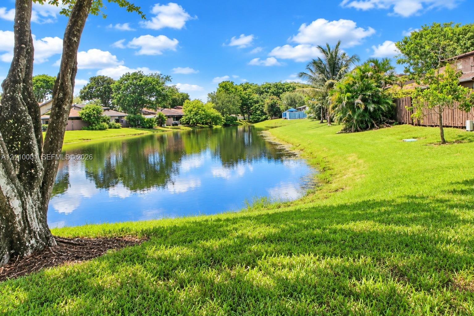 Waterfront lot featuring a grass lawn, mature trees, and wooden fencing
