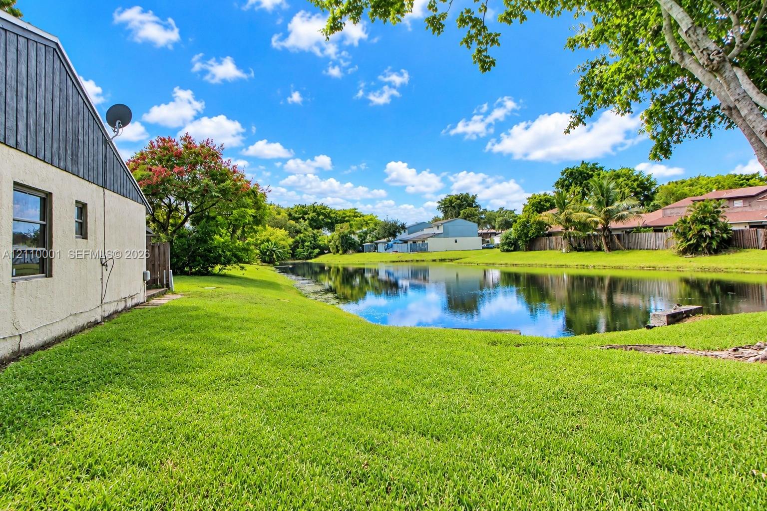 Waterfront backyard featuring a manicured lawn, perimeter wood fencing, and mature landscaping