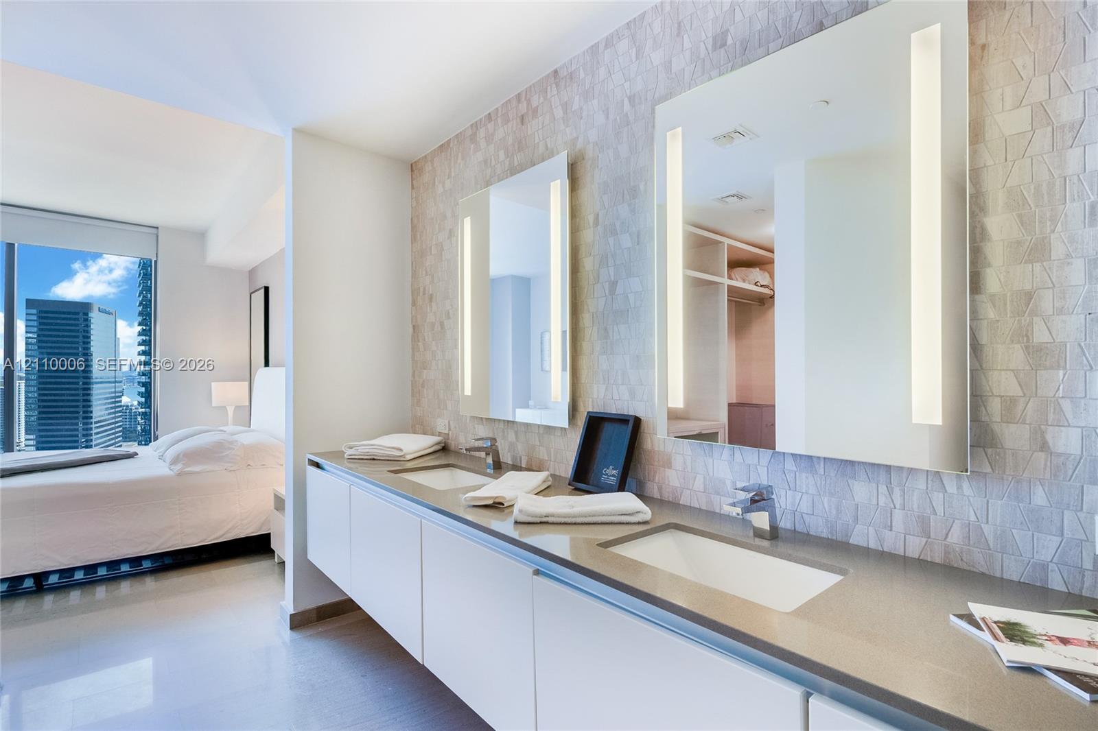 Floating dual-sink vanity with a solid surface countertop, textured tile accent wall, and frameless integrated LED mirrors