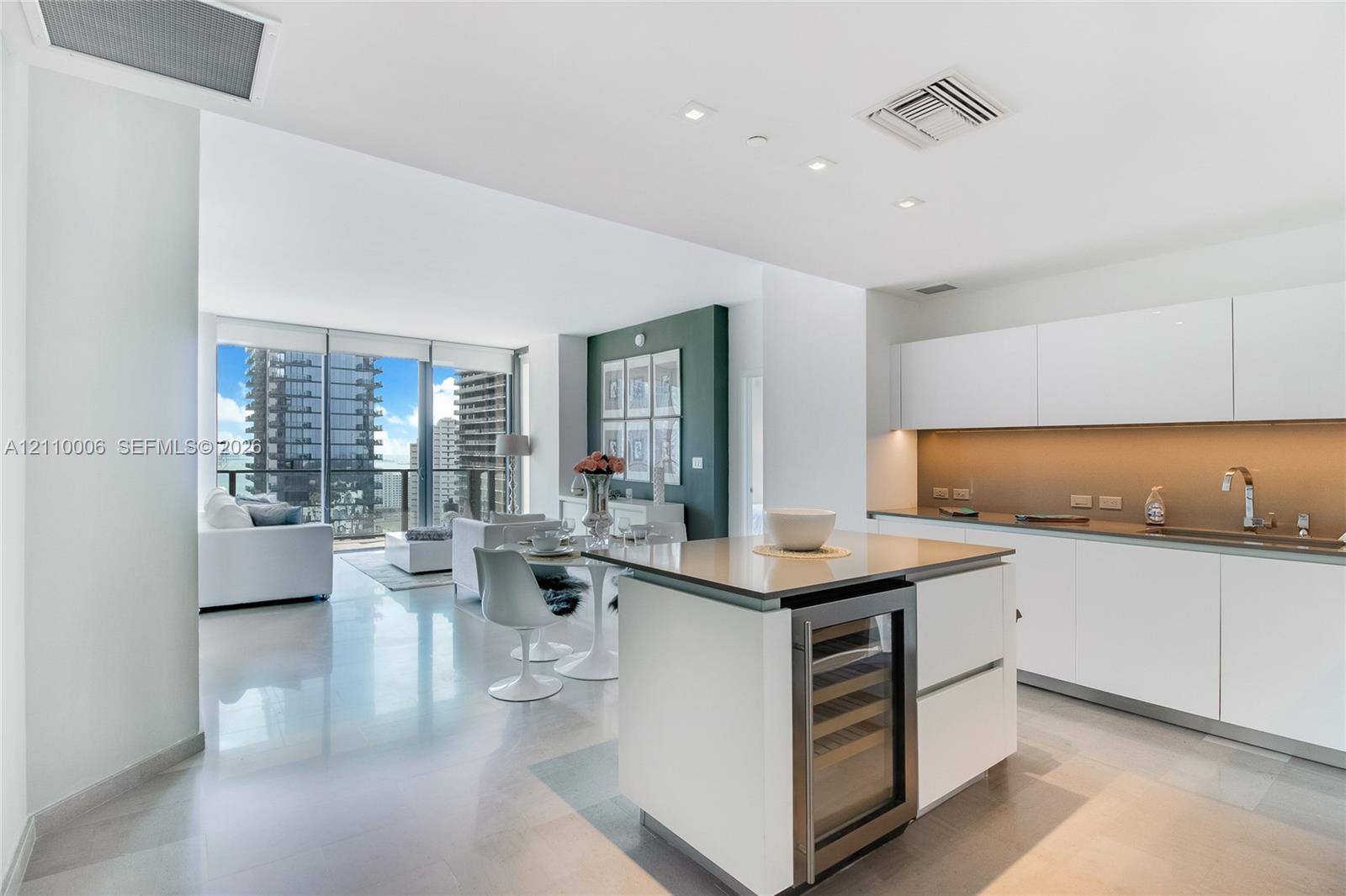 Modern kitchen featuring high-gloss white cabinetry, integrated stainless steel appliances, built-in wine cooler, stone-finish countertops, and polished large-format flooring