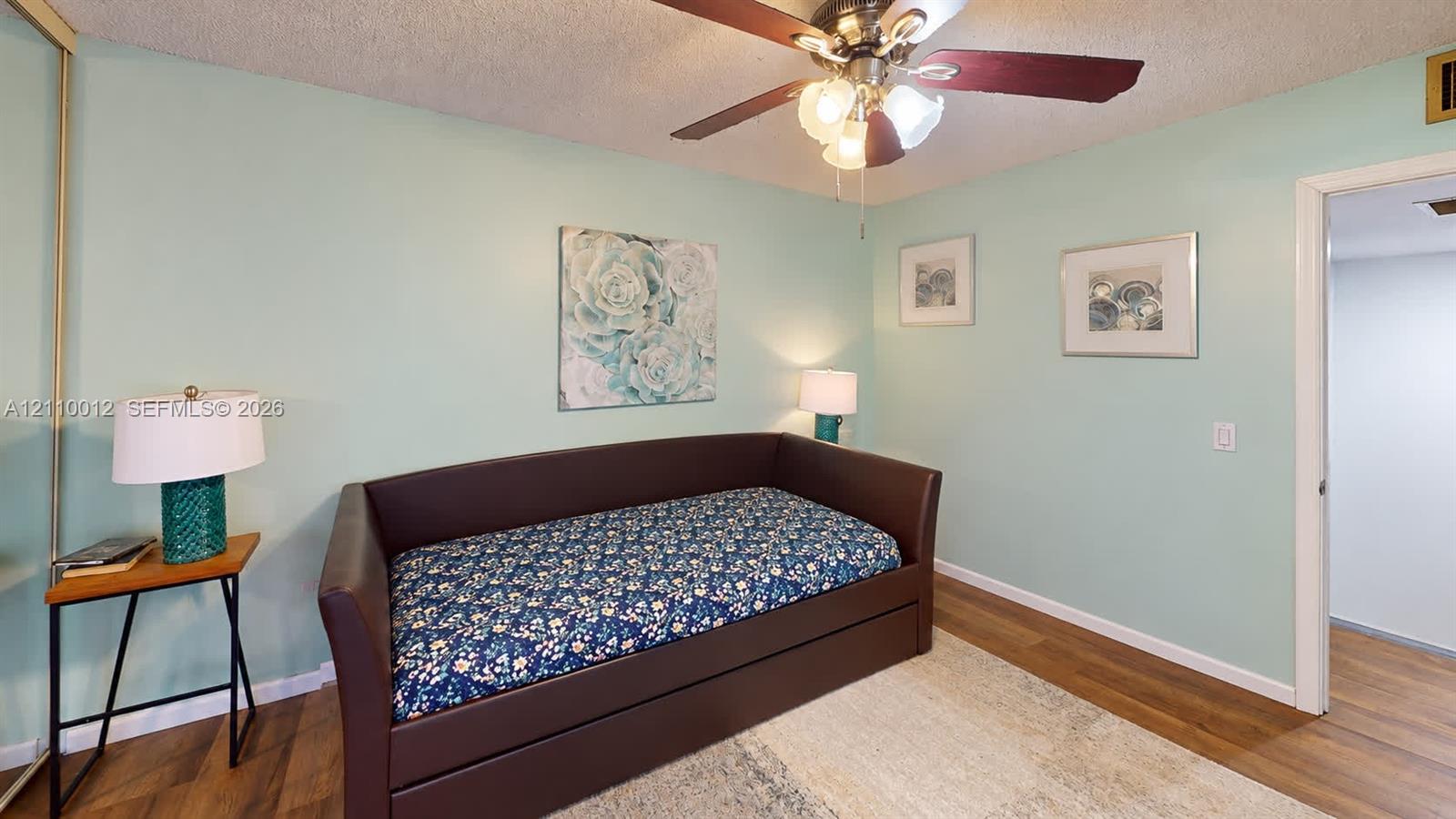 Room featuring wood-finish flooring, a ceiling fan with integrated lighting, and a floor-to-ceiling mirrored closet door