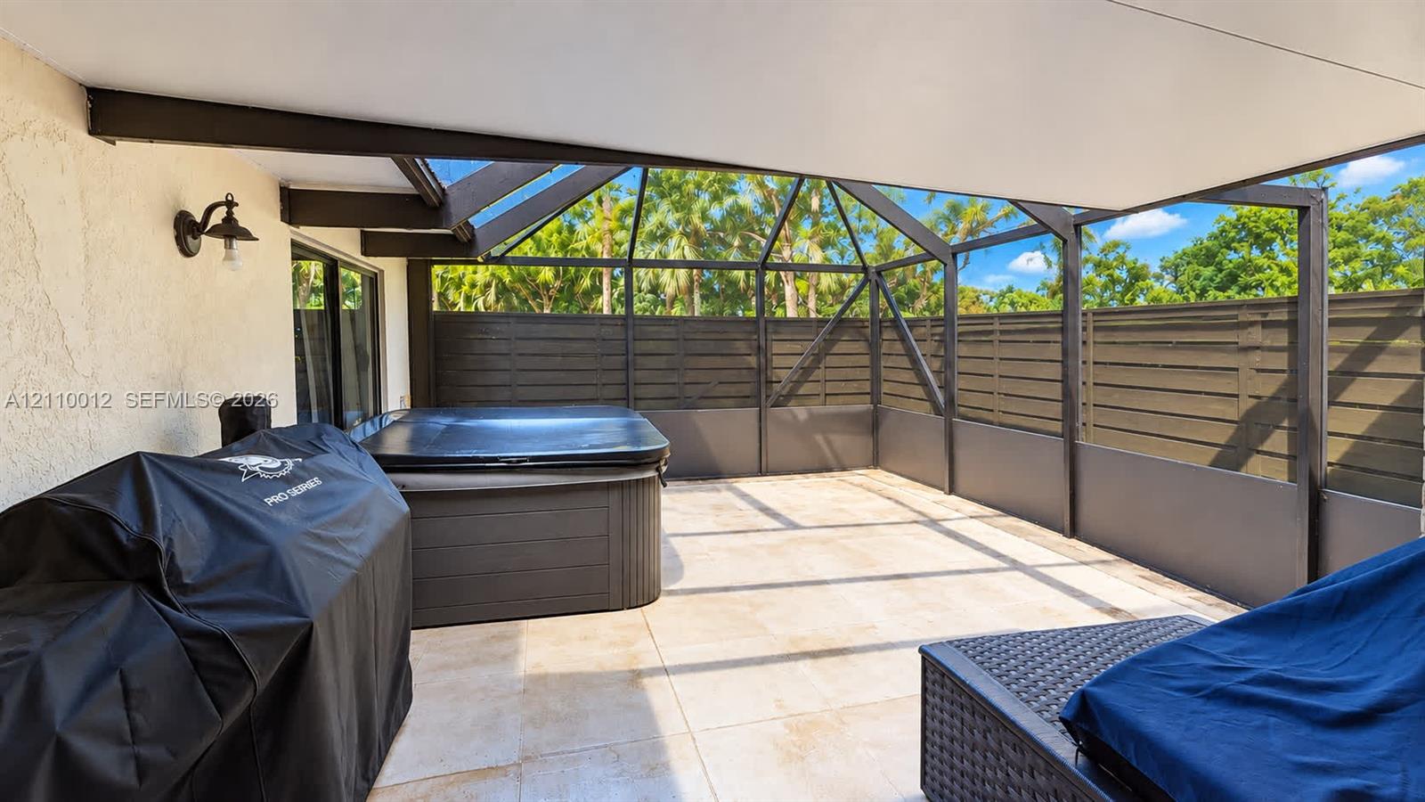 Screened-in patio featuring tiled flooring, a built-in spa, privacy fencing, and a wall-mounted exterior light fixture