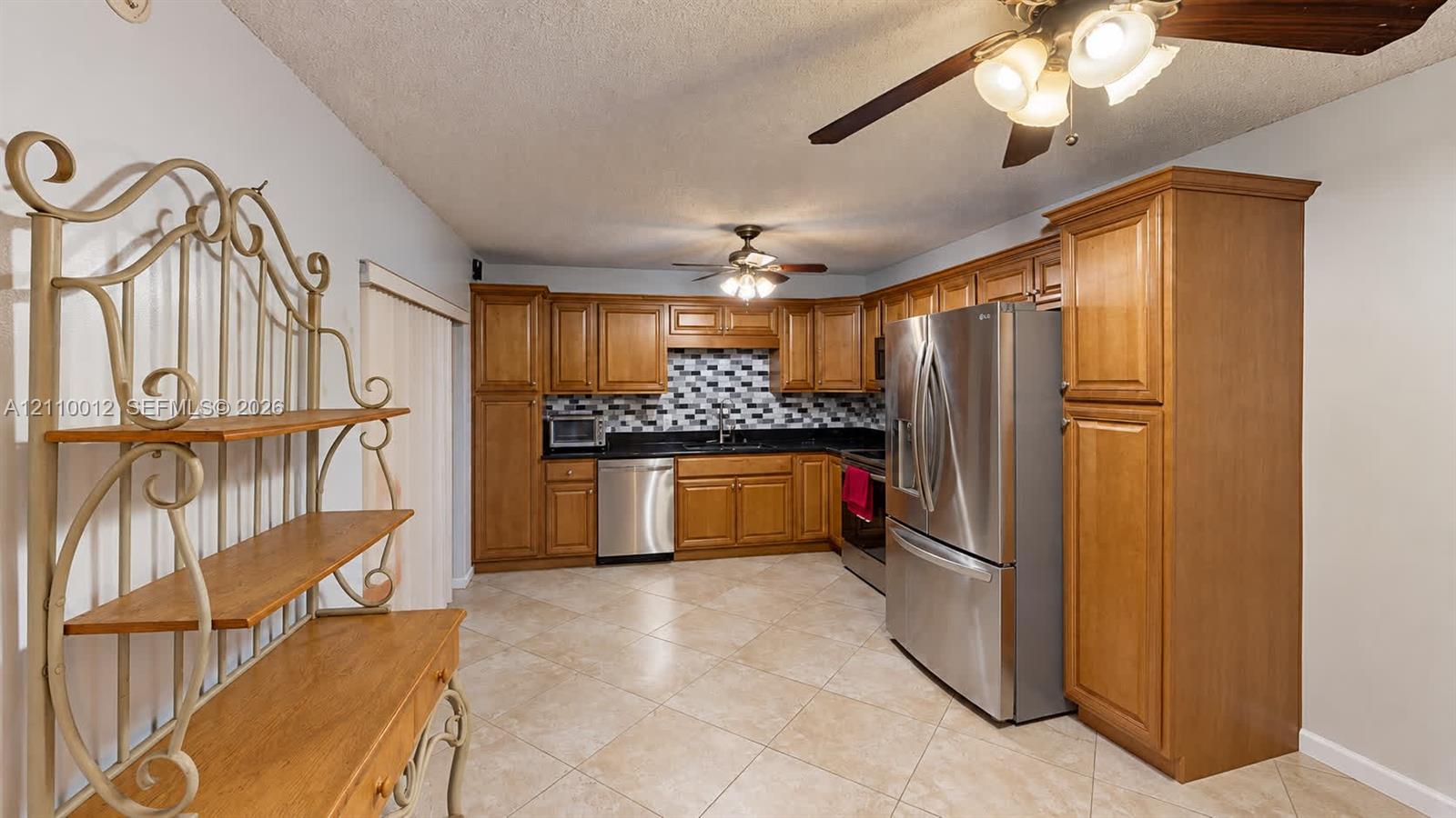 Kitchen featuring wooden cabinetry, dark countertops, a mosaic tile backsplash, stainless steel appliances, and ceramic tile flooring