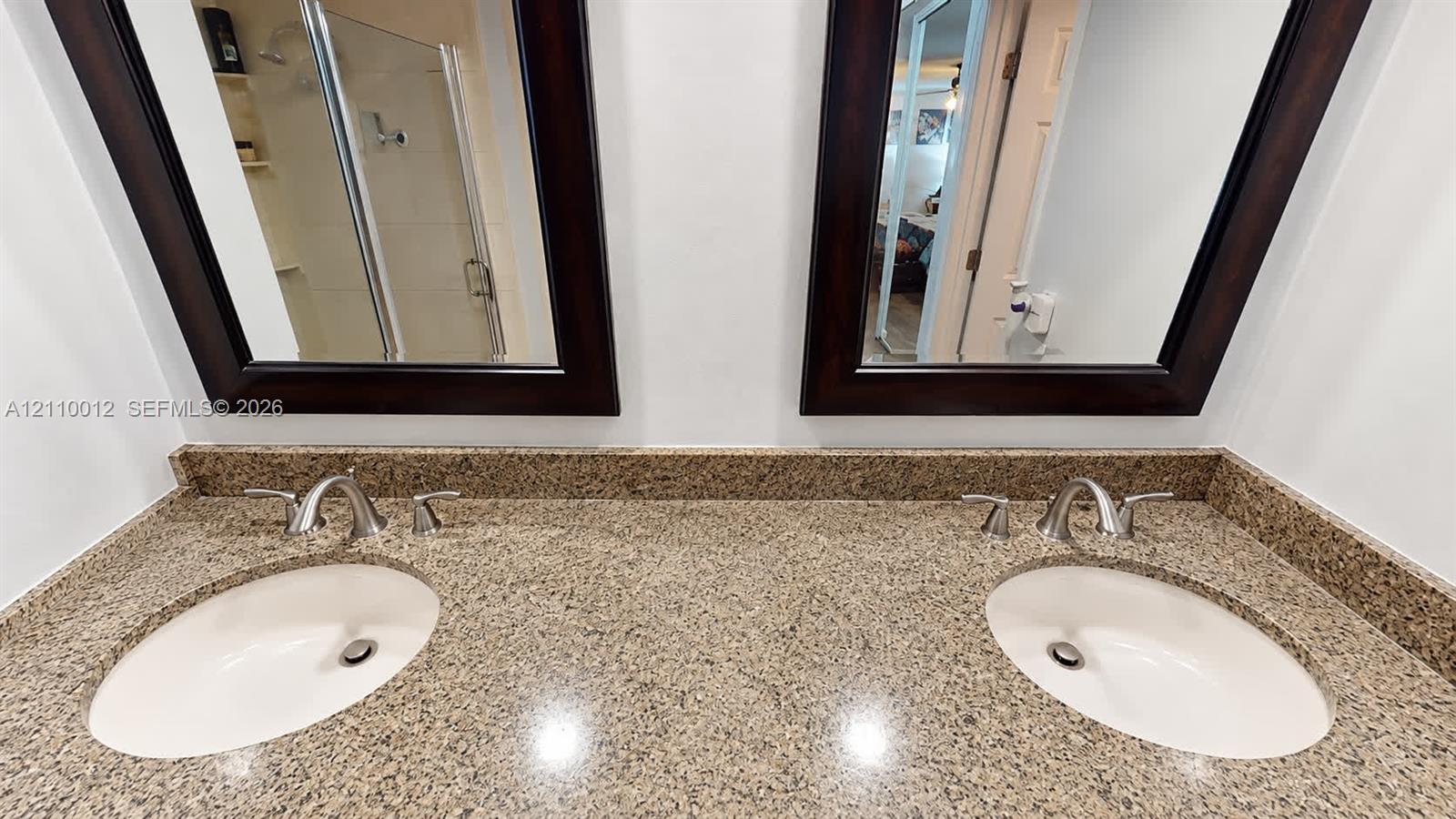 Double vanity featuring stone countertops, dual undermount sinks, polished chrome widespread faucets, and two dark-finished framed wall mirrors