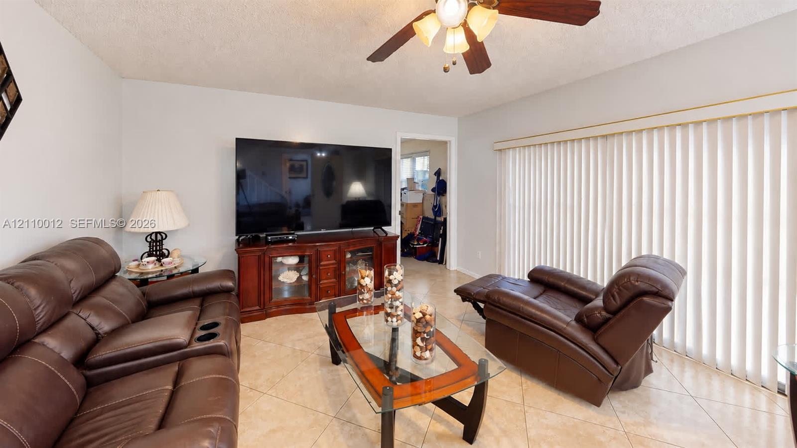 Neutral tile flooring, ceiling fan with light fixture, and vertical window blinds