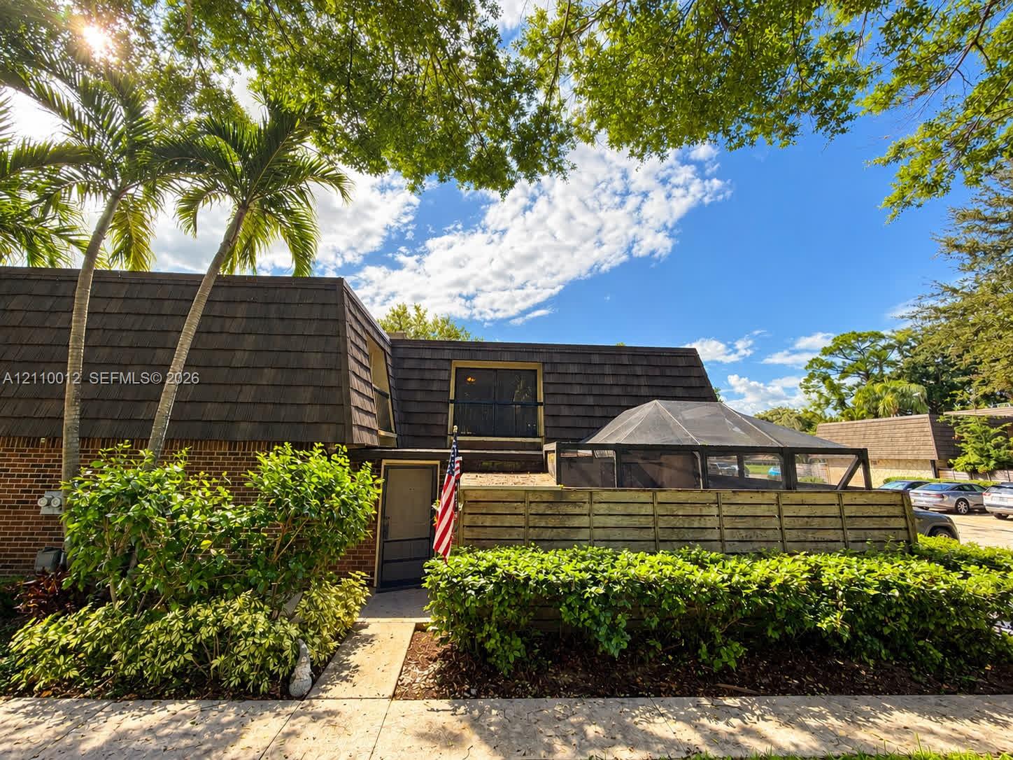 Exterior featuring brick masonry, dark shingled mansard roofline, screened-in enclosure, and mature landscaping