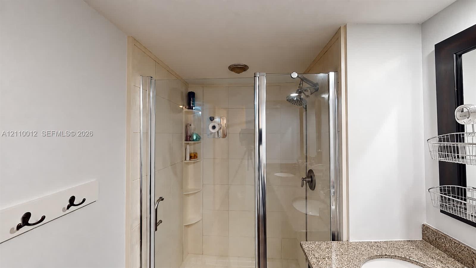 Walk-in shower featuring a frameless glass door, neutral-toned wall tile, and integrated corner shelving, complemented by a vanity with a stone-finish countertop