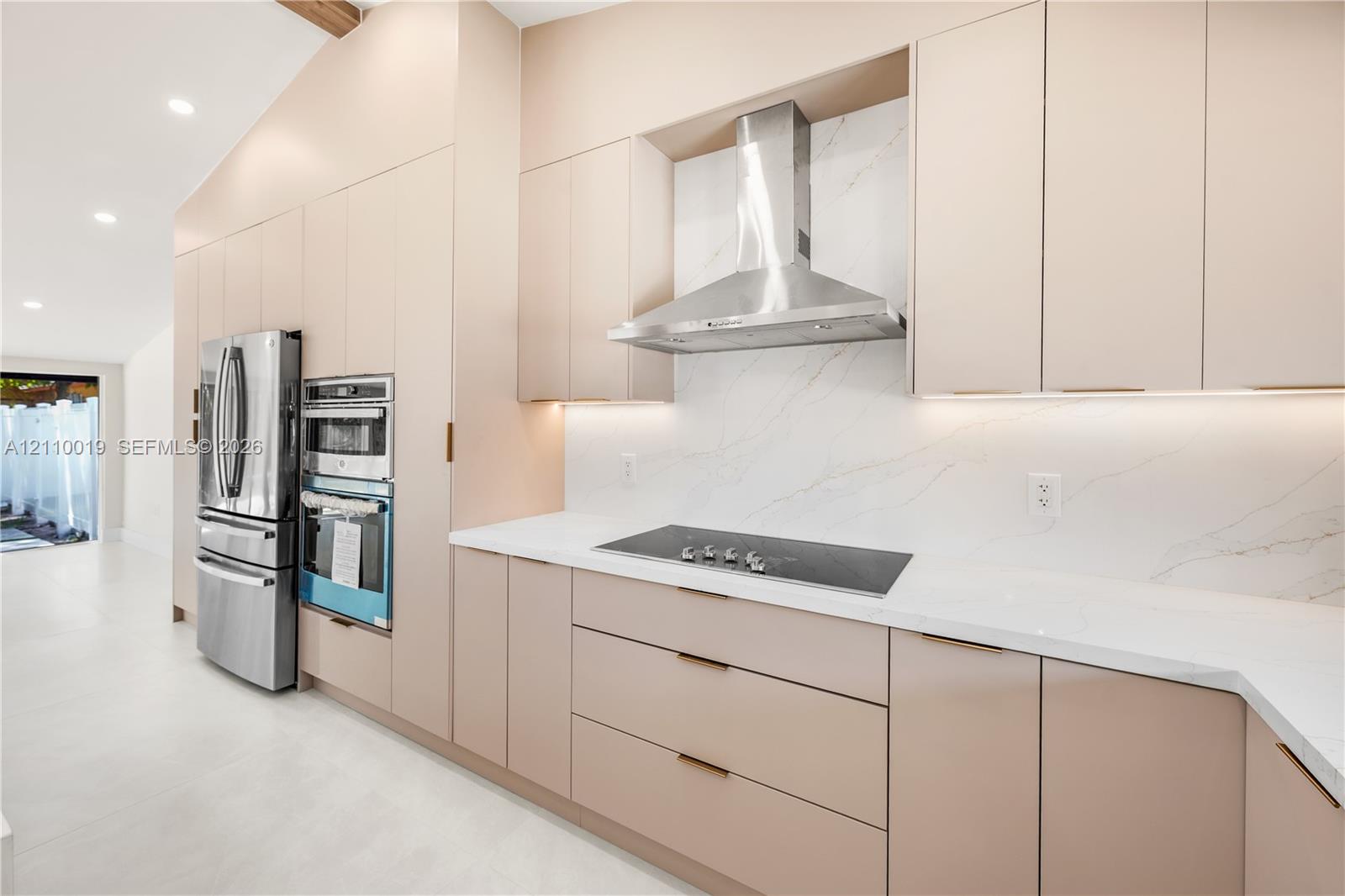 Custom flat-panel cabinetry, stone-surface countertops, full-height stone backsplash, stainless steel built-in double wall ovens, and stainless steel chimney range hood