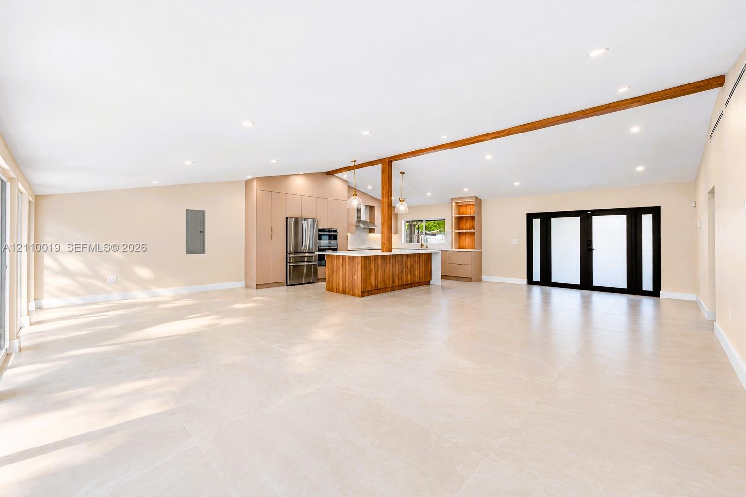 Expansive open-concept interior featuring vaulted ceilings, large-format tile flooring, a wood-accented center island, built-in cabinetry, and black-framed multi-panel glass doors