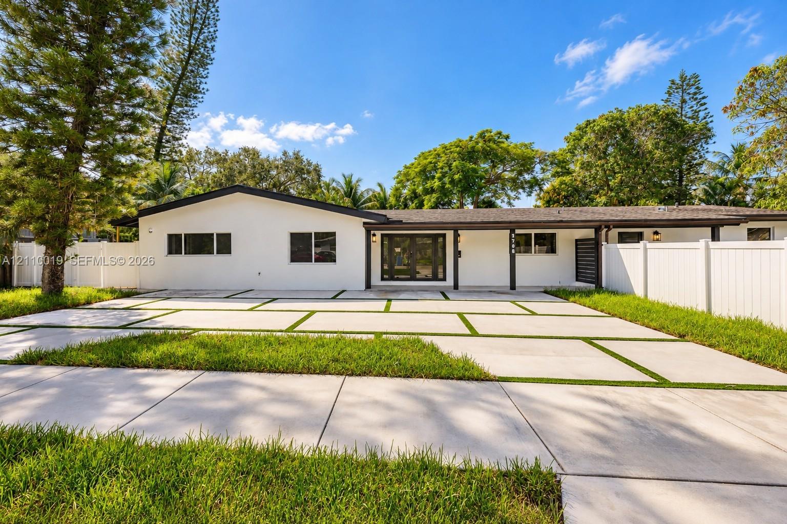 Single-story exterior featuring white stucco siding, a concrete paver driveway with turf accents, a covered porch, and privacy fencing