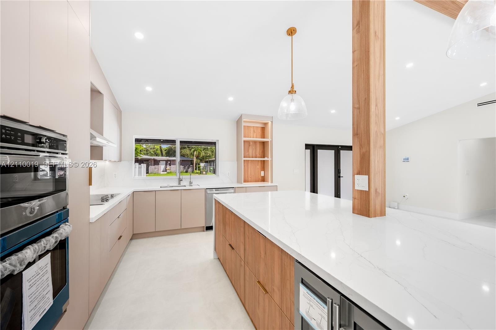 Kitchen featuring flat-panel cabinetry, a spacious stone-surfaced island, integrated stainless steel appliances, a structural wood pillar, and recessed lighting