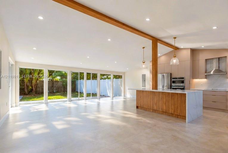 Open-concept space featuring an exposed wood structural beam, floor-to-ceiling sliding glass doors, a large kitchen island with stone-finish waterfall edges, flat-panel cabinetry, and recessed lighting