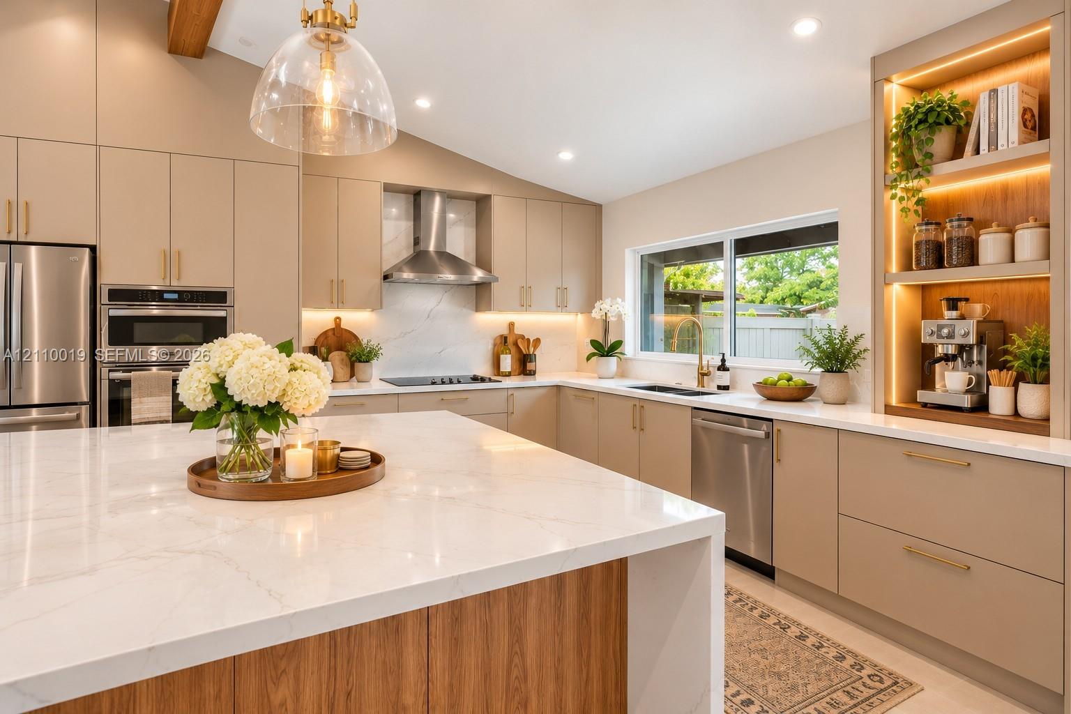 Kitchen featuring an oversized waterfall island with stone countertop, flat-panel cabinetry, stainless steel appliances, a built-in illuminated display nook, and vaulted ceiling