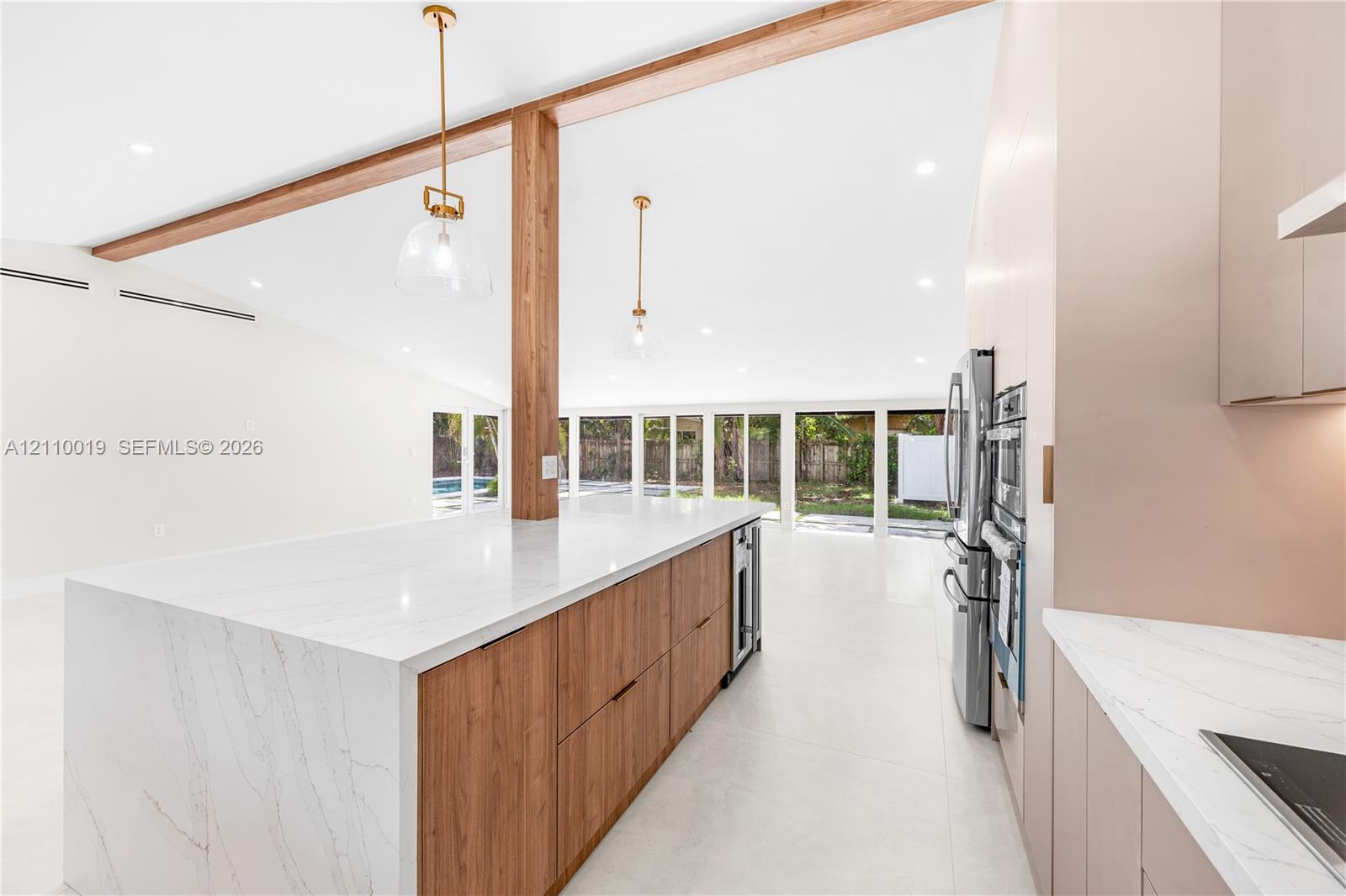 Kitchen featuring a waterfall-edge stone countertop, wood-finish cabinetry, exposed wood ceiling beams, pendant lighting, and stainless steel built-in appliances