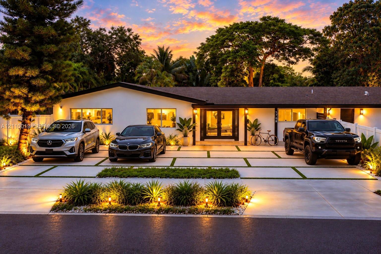 Single-story residence featuring a low-pitched roofline, light-toned exterior finish, segmented concrete driveway with grass inlays, and mature landscaping