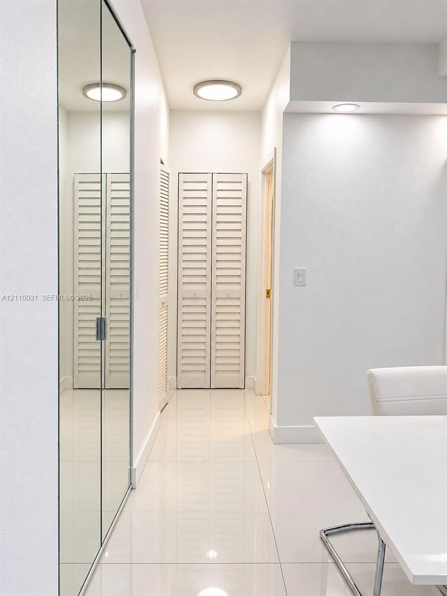 Hallway featuring floor-to-ceiling mirrored sliding closet doors, white louvered bifold closet doors, high-gloss tile flooring, and flush-mount ceiling lighting