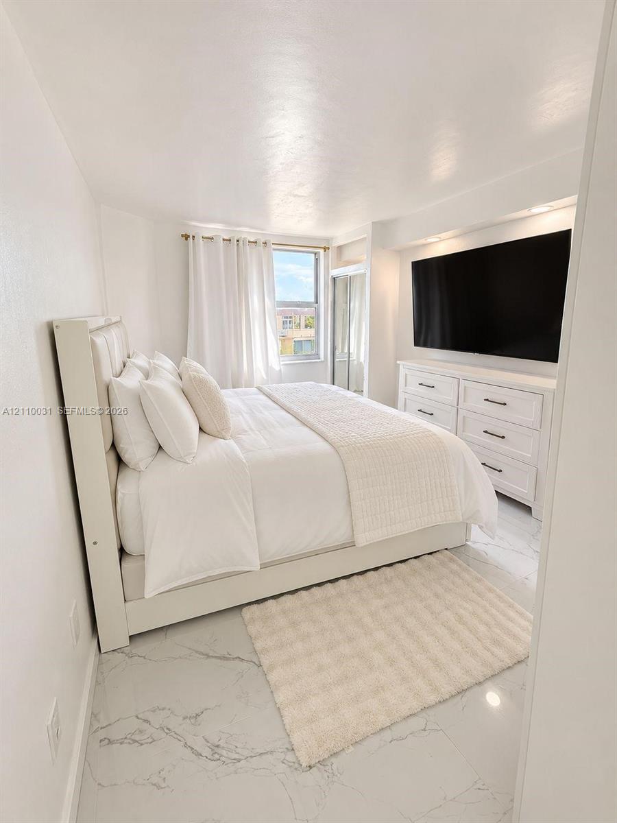 Large-format white tile flooring with grey veining, recessed lighting, and a floor-to-ceiling mirrored closet door