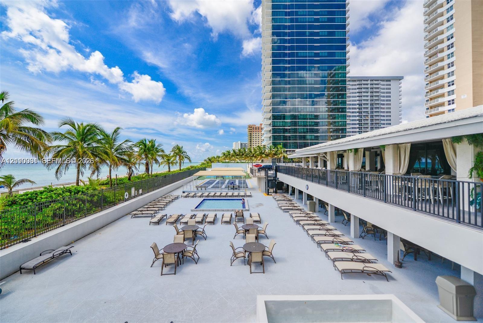 Expansive pool deck featuring a rectangular swimming pool, integrated metal railings, and a covered terrace with structural columns