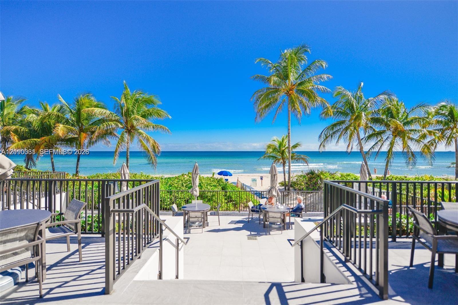 Outdoor patio featuring light-toned tile flooring, black metal railings, and a direct oceanfront setting with mature palm trees