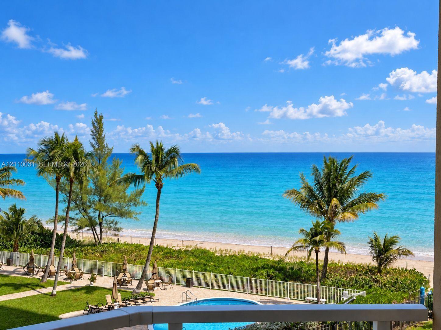 Balcony with direct ocean horizon, private swimming pool, fenced perimeter, and manicured landscaping overlooking the beach