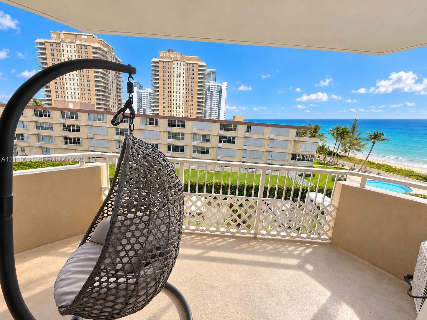 Private balcony featuring a textured concrete floor, white metal railing, and direct sightlines to the ocean and coastline