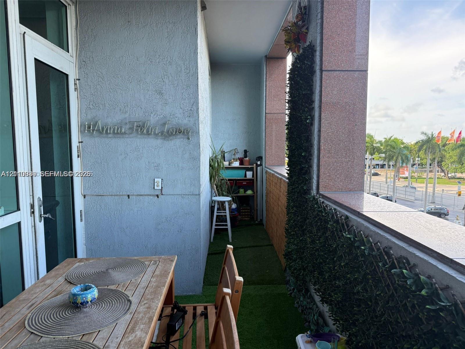 Covered balcony featuring textured stucco walls, polished stone-finish railing, and green synthetic turf flooring