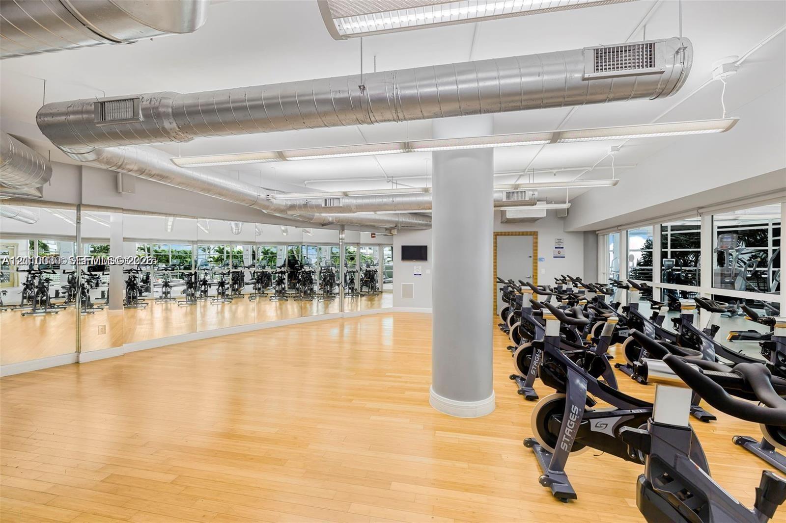 Industrial aesthetic featuring exposed metal ductwork, full-wall mirrors, light wood-finish flooring, and linear LED lighting