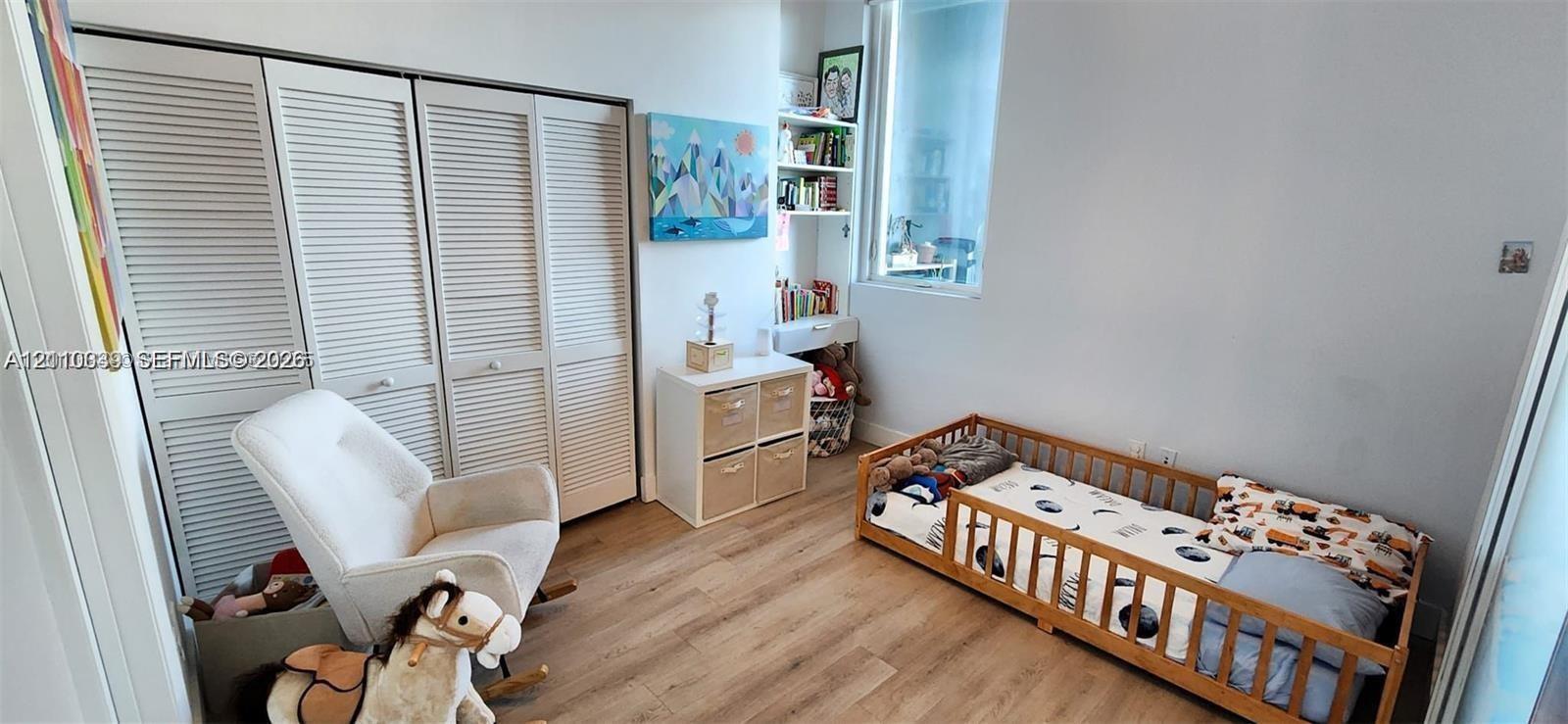 Interior room featuring light-toned wood-finish flooring, floor-to-ceiling louvered-panel closet doors, and a built-in white shelving unit