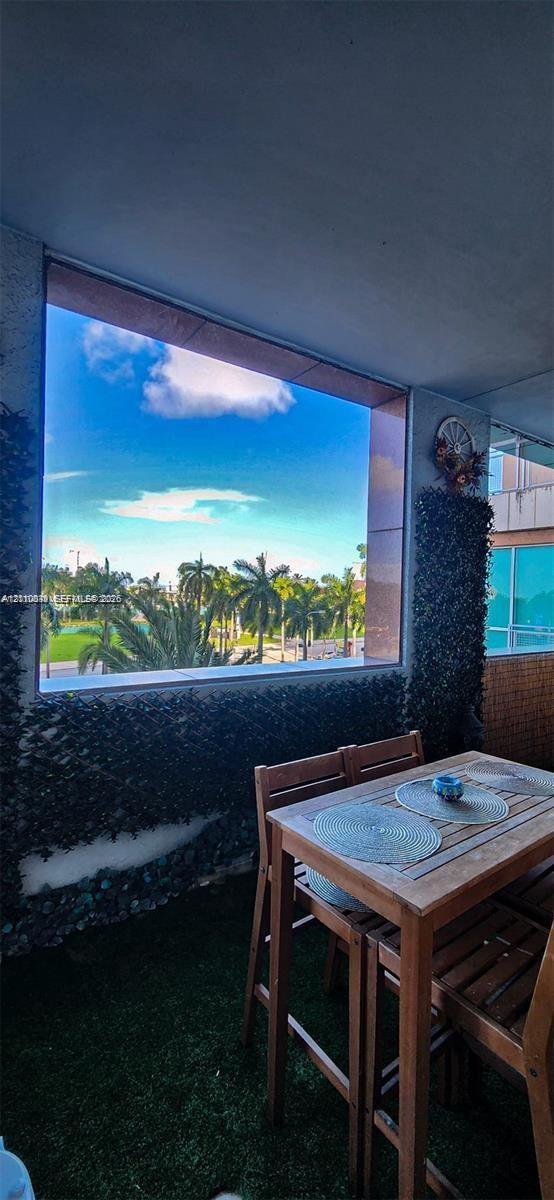 Covered balcony featuring artificial turf flooring, accent walls adorned with greenery, and a large fixed-pane window with exterior landscape imagery