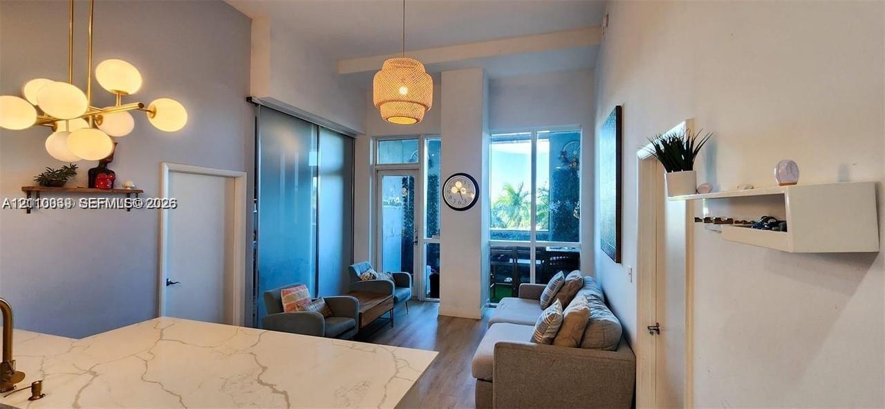 High-ceiling interior featuring a gold-finish multi-globe chandelier, a woven pendant light, expansive floor-to-ceiling windows, and a countertop with stone-patterned surfacing High-ceiling interior featuring a gold-finish multi-globe chandelier, a woven pendant light, expansive floor-to-ceiling windows, and a countertop with stone-patterned surfacing