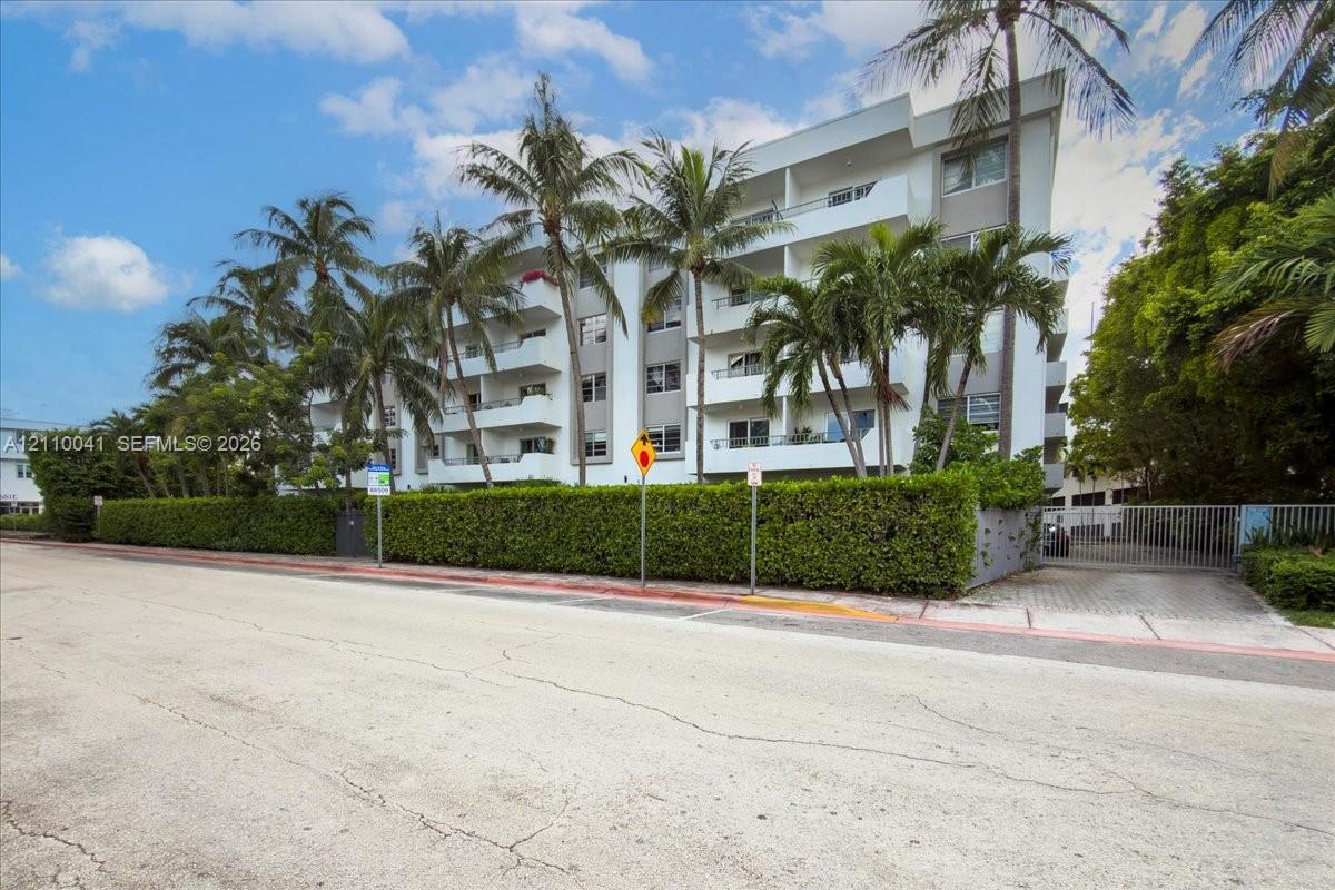 Multi-story building featuring private balconies, a gated entrance, and landscaped perimeter hedging