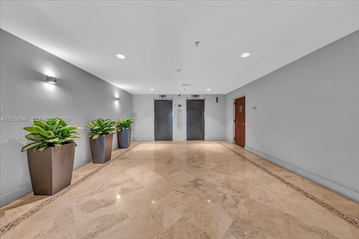 Common area lobby featuring polished stone flooring with decorative inlay, dual elevator banks, and recessed ceiling lighting