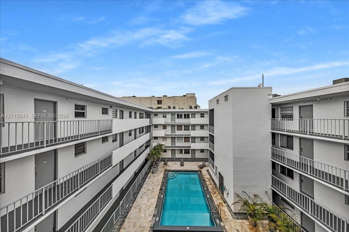 Rectangular swimming pool featuring a stone-paver deck and surrounding multi-story building exterior with metal balcony railings