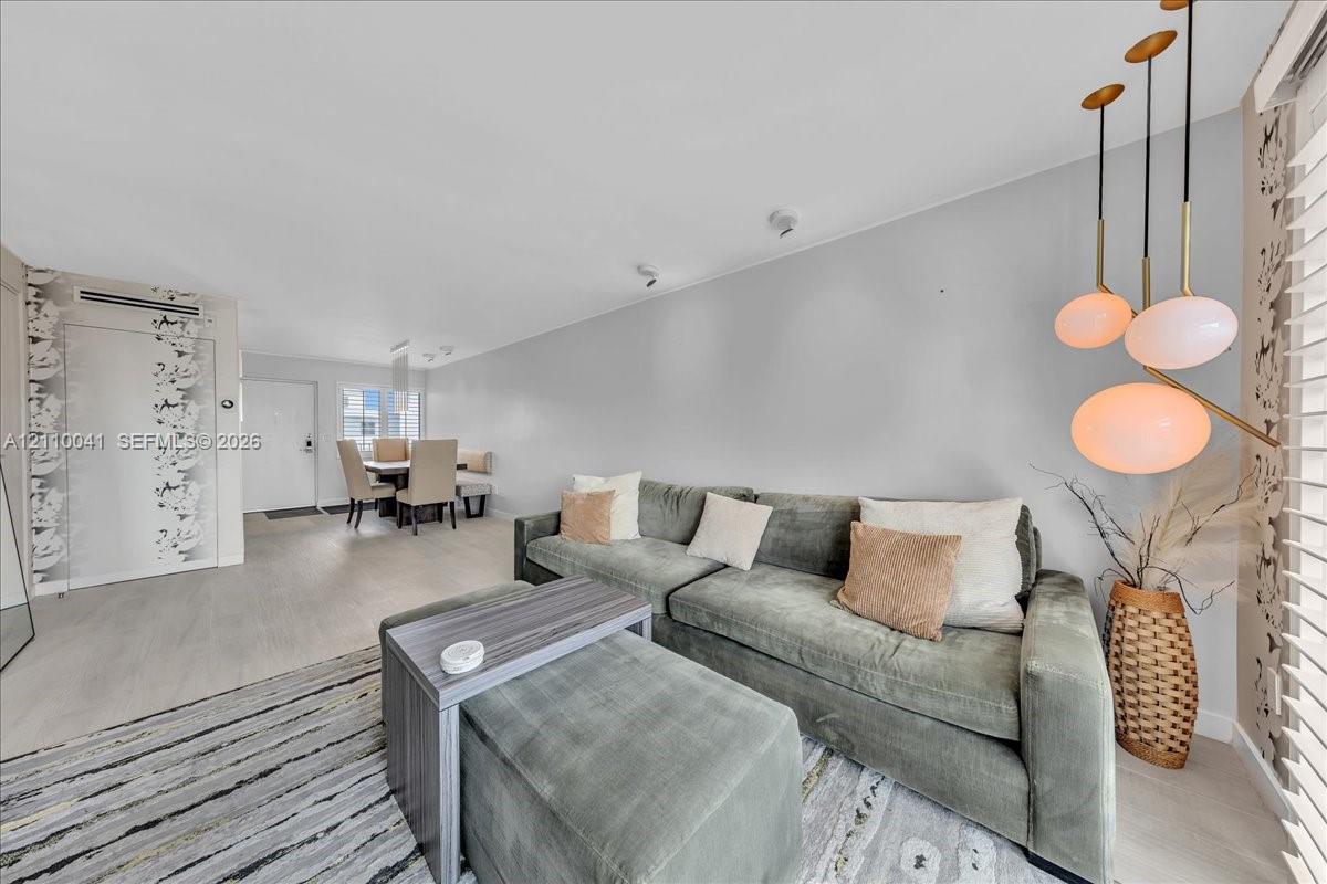 Multi-pendant brass light fixture, wood-finish flooring, patterned wallpaper accent wall, and horizontal window blinds