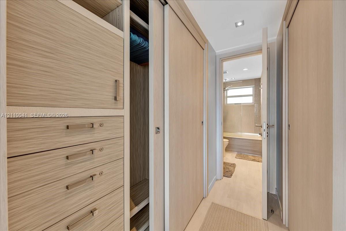 Built-in wood-finish cabinetry featuring integrated drawers, sliding closet doors, recessed ceiling lighting, and polished metal hardware