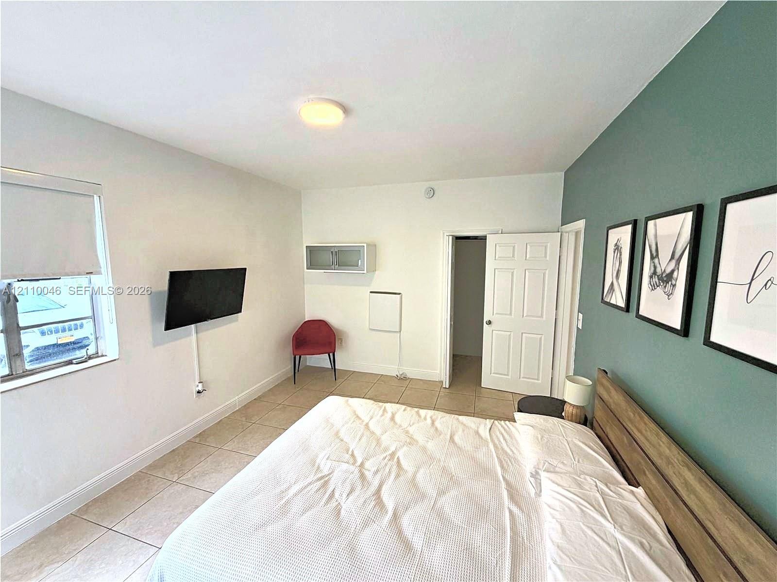 Room featuring ceramic tile flooring, a dual-tone wall design with an accent wall, a built-in overhead storage cabinet, and a six-panel interior door