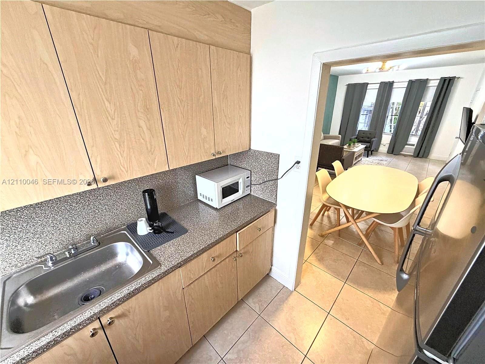 Kitchen featuring light wood-finish cabinetry, speckled laminate countertops, a stainless steel basin sink, and tile flooring