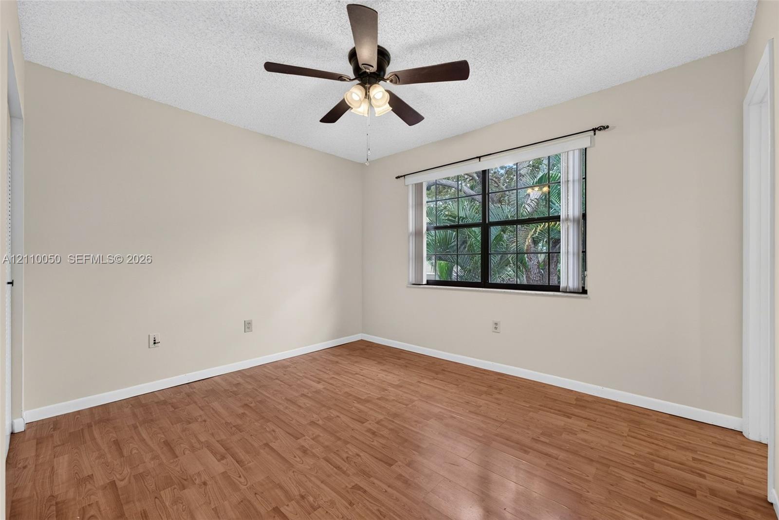 Room featuring wood-finish flooring, a multi-pane window, and a ceiling fan with integrated lighting